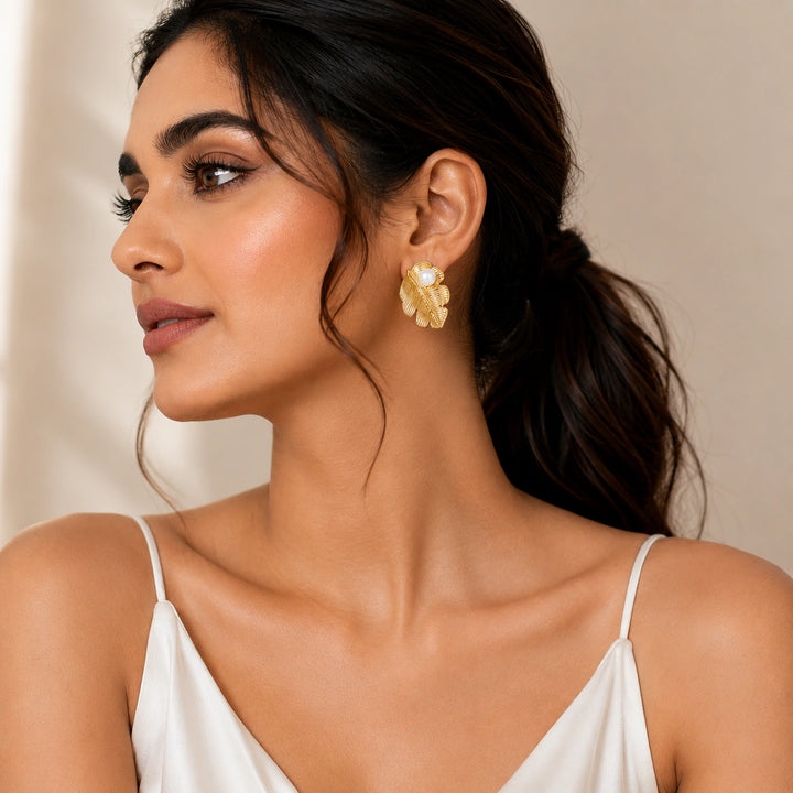 Gold ribbed leaf pearl studs on a dark jewellery studio display