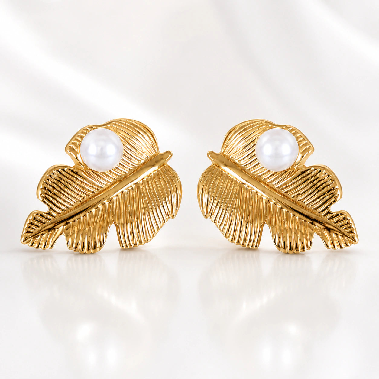 Gold ribbed leaf pearl studs styled in an elegant jewellery flat lay