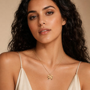 Gold sculpted bow charm necklace on a dark jewellery studio display