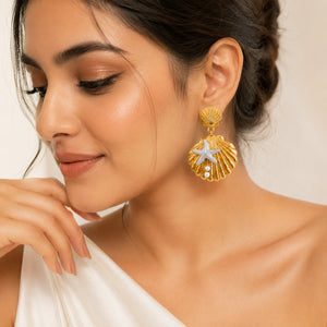 Gold shell starfish pearl earrings on a dark jewellery studio display