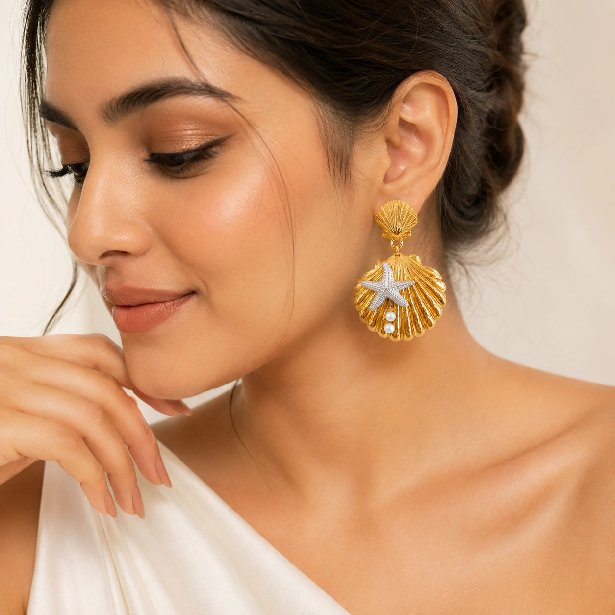 Gold shell starfish pearl earrings on a dark jewellery studio display
