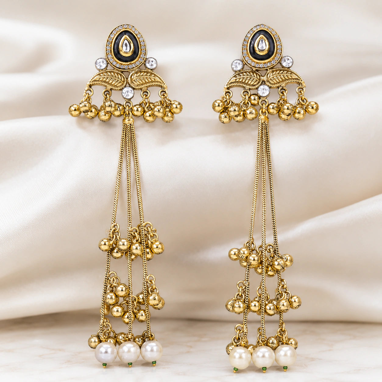 Angled view of gold-tone Kundan-style earrings with pearl-style tassel drops