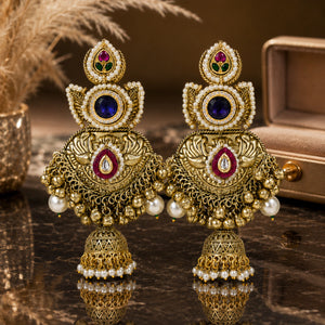 Gold-tone Kundan-style pearl jhumka earrings on a glossy dark reflective display