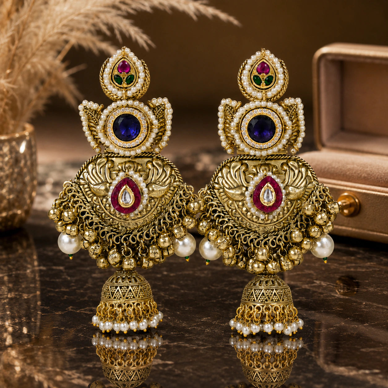 Gold-tone Kundan-style pearl jhumka earrings on a glossy dark reflective display