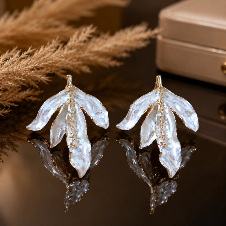 Pearl-white sculptural leaf earrings on a dark jewellery studio display
