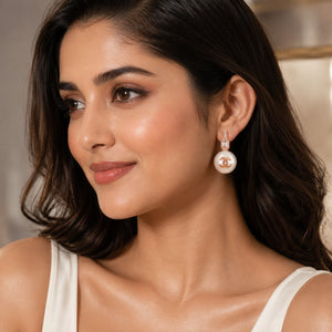 Rose-gold pearl emblem drop earrings on a dark jewellery studio display